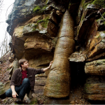 David Rives standing by a tree fossil extending through many layers of rock