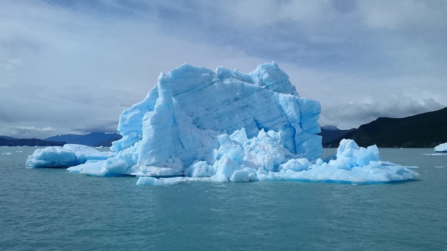 Blue-tinged iceberg with mountains in backdrop, photo credit: Pxhere